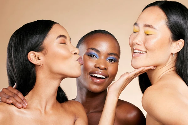 Trzy kobiety o odmiennych karnacjach ale promiennych cerach uśmiechają się do siebie